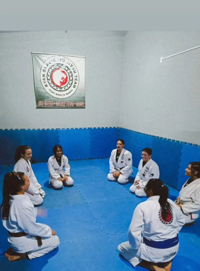 Grupo de praticantes de jiu-jitsu sentados em roda sobre o tatame azul