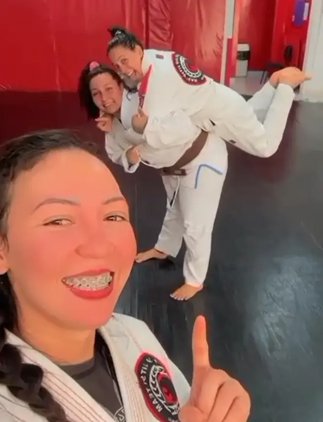 Tamires França em pé com kimono preto e faixa azul em ambiente de treino